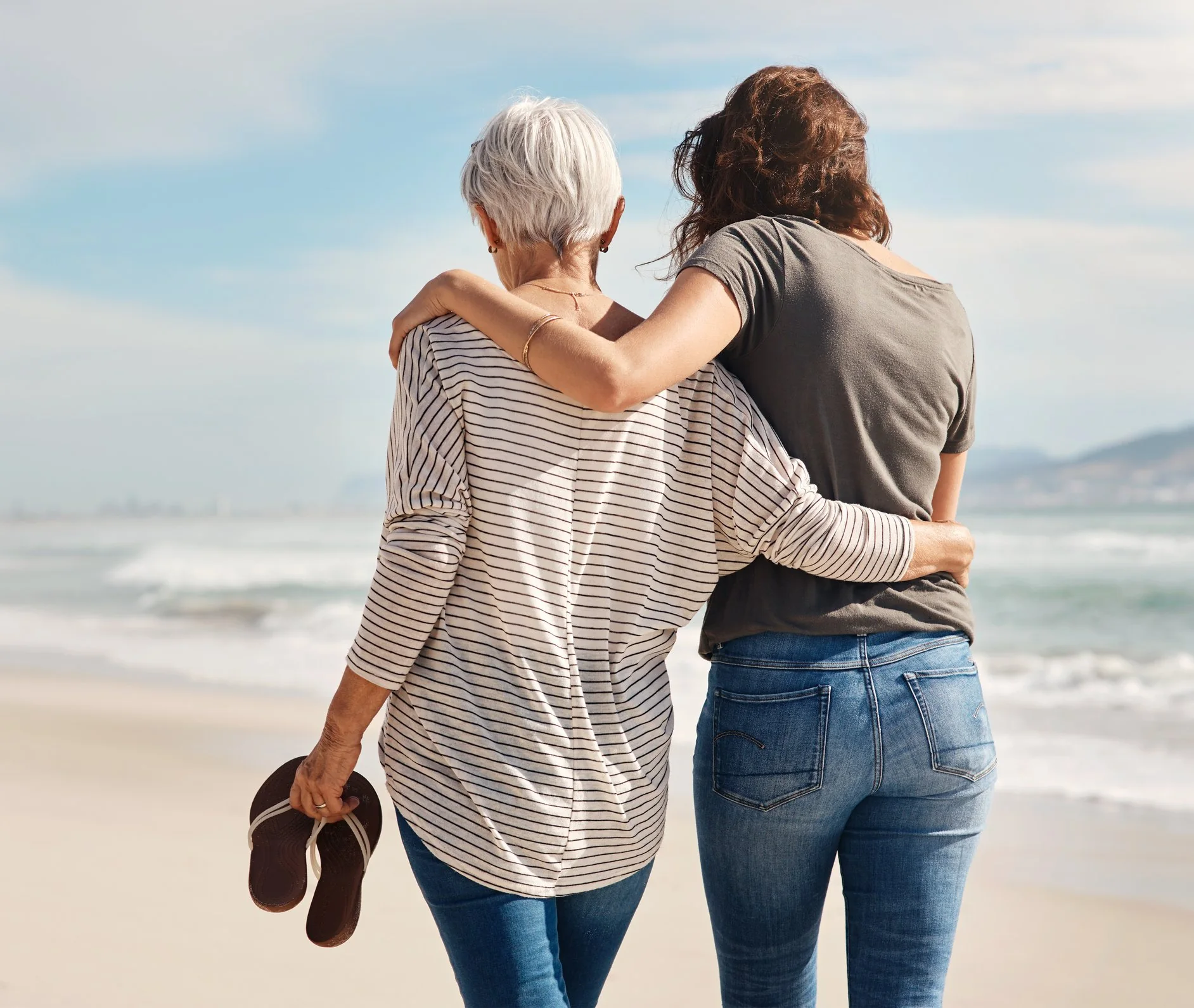 An older and a younger woman walking on the beach holding each other