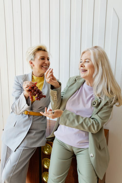 Older woman making her friend laugh while holding a bundle of grapes.