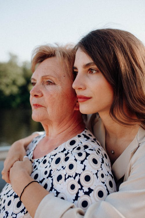 Adult woman hugging her mother while leaning over her shoulder.