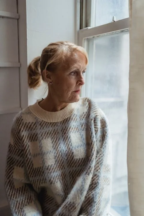 Sad older woman looking out of her window.