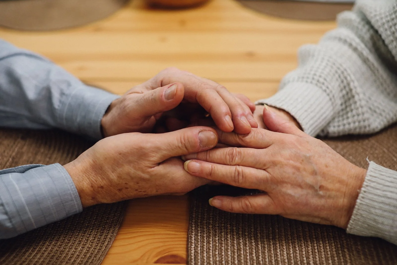 Close-up shot of an elderly couple holding hands on top of a wooden table.